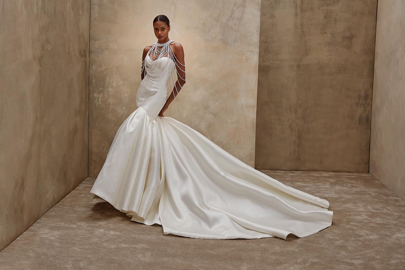 Eine Frau mit ernstem Blick steht in elegantem, weiss glänzendem Brautkleid