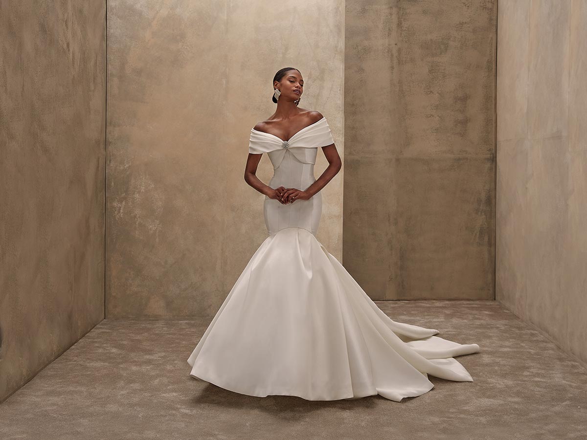 Elegante Frau im weißen Brautkleid steht lächelnd vor beigefarbenem Hintergrund