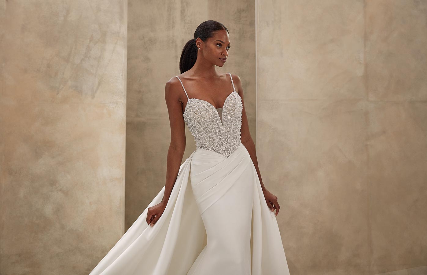 Eine Frau mit ruhigem Blick trägt ein weißes Brautkleid mit Perlendetails