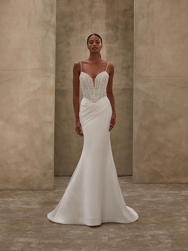 Junge Frau im weißen Brautkleid mit Perlen, ernst blickend vor beigem Hintergrund