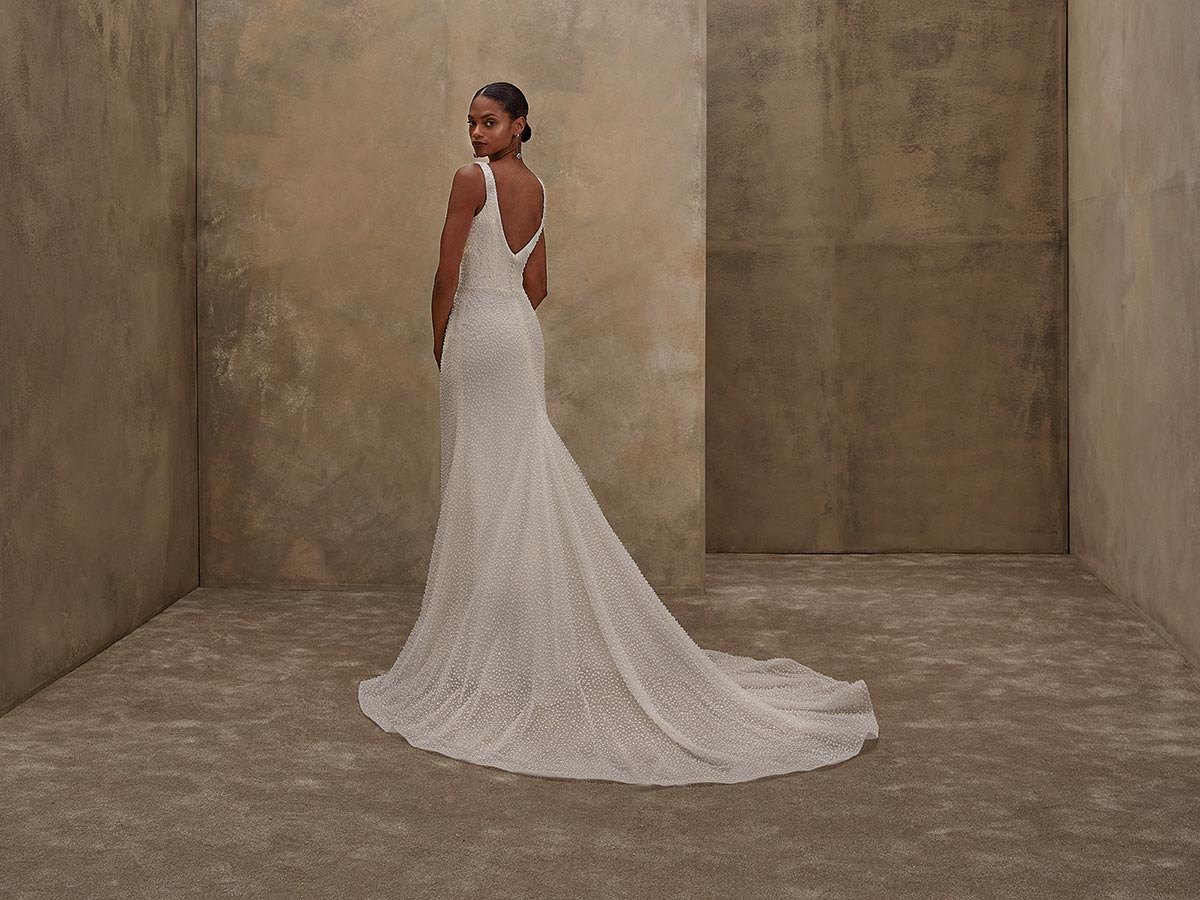 Eine elegante Frau im weißen Brautkleid mit Schleppe blickt lächelnd über die Schulter