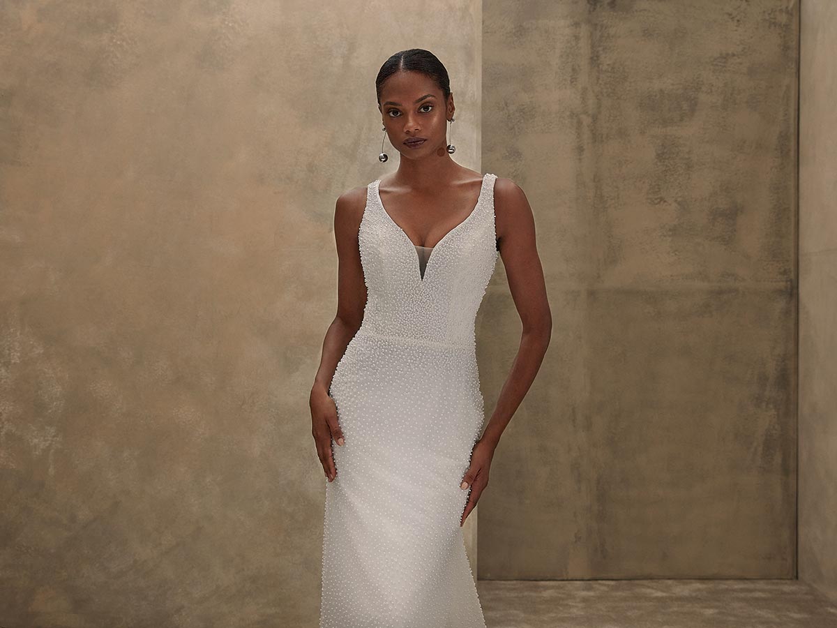 Eine elegant gekleidete Frau im weißen Kleid blickt ernst in die Kamera vor Betonwand