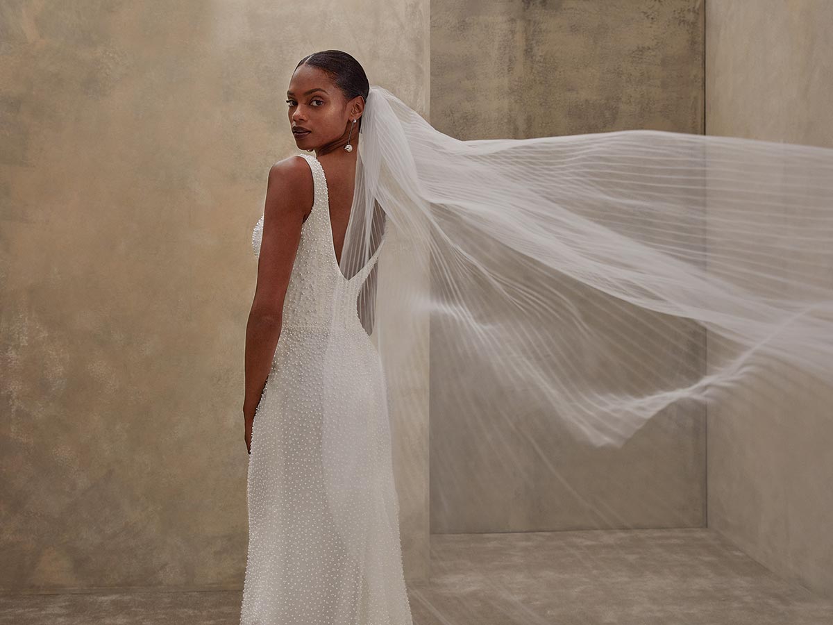 Eine elegant gekleidete Frau im weißen Brautkleid mit langem Schleier blickt ernst