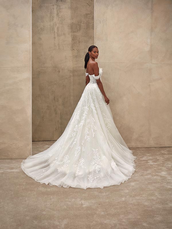 Eine elegante Frau mit ernster Miene trägt ein weißes Spitzenbrautkleid mit langer Schleppe