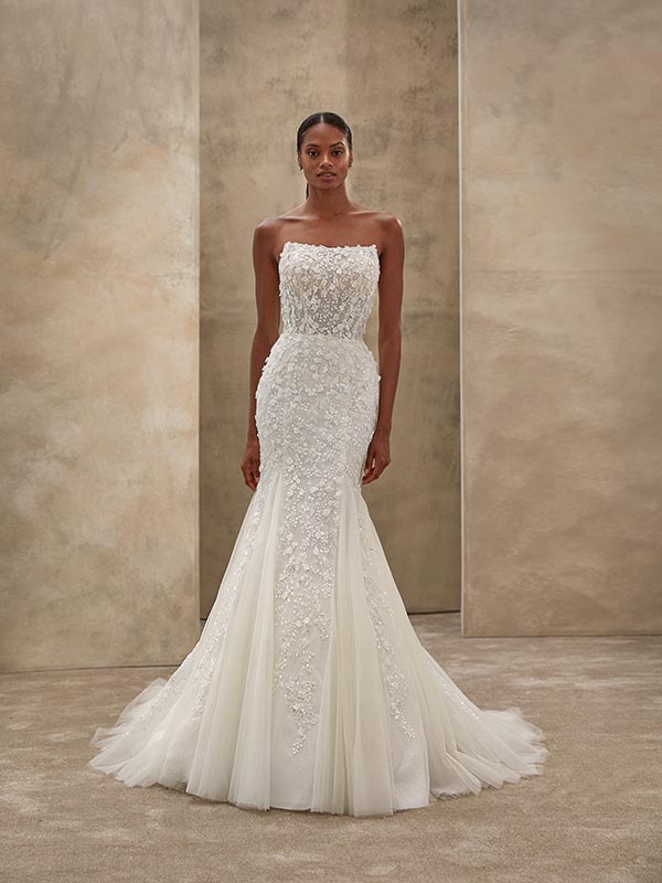 Eine elegante Frau mit neutralem Ausdruck trägt ein weißes, blumiges Brautkleid