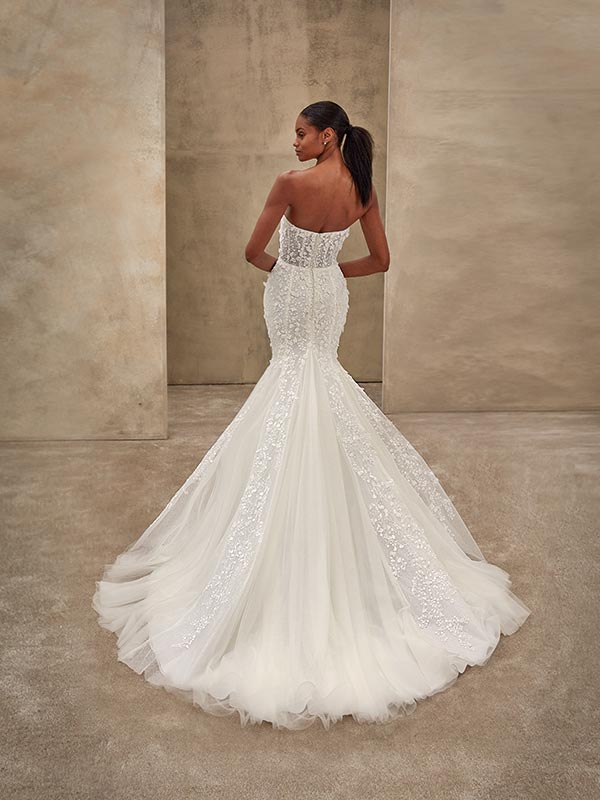 Eine Frau im eleganten weißen Hochzeitskleid steht lächelnd mit dem Rücken zur Kamera