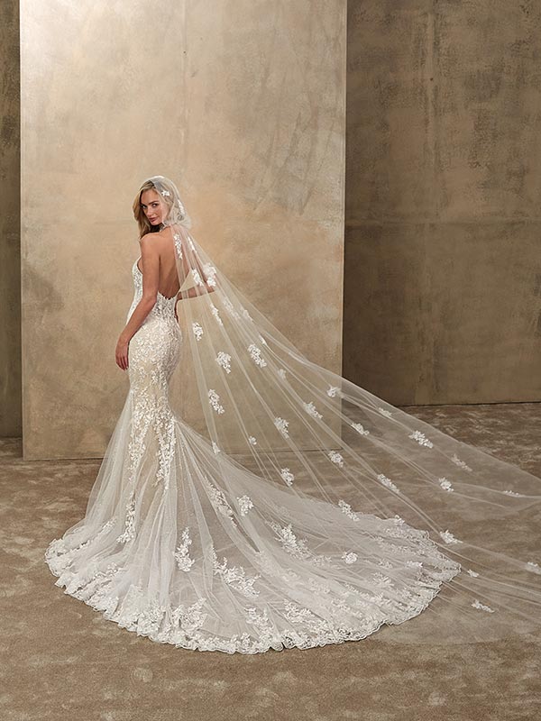 Eine lächelnde Frau trägt ein elegantes Spitzenbrautkleid mit langer Schleppe in Weiß