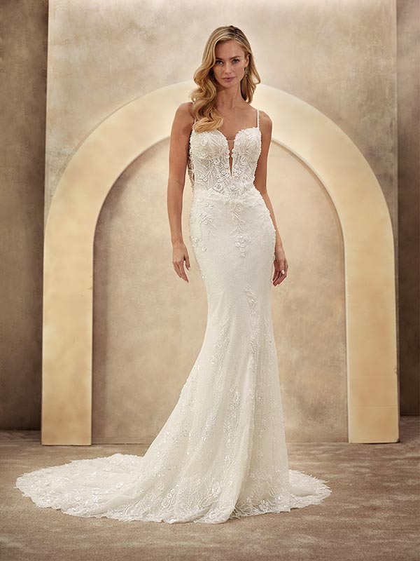 Eine blonde Frau lächelt dezent und trägt ein elegantes, figurbetontes Brautkleid in Weiß