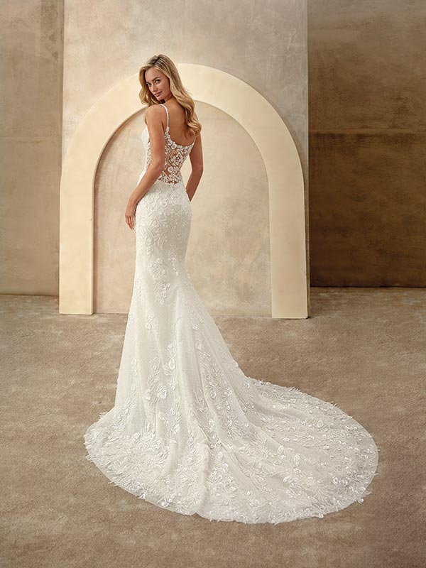 Blonde Frau mit elegantem Lächeln trägt ein cremeweißes Spitzenbrautkleid mit Schleppe