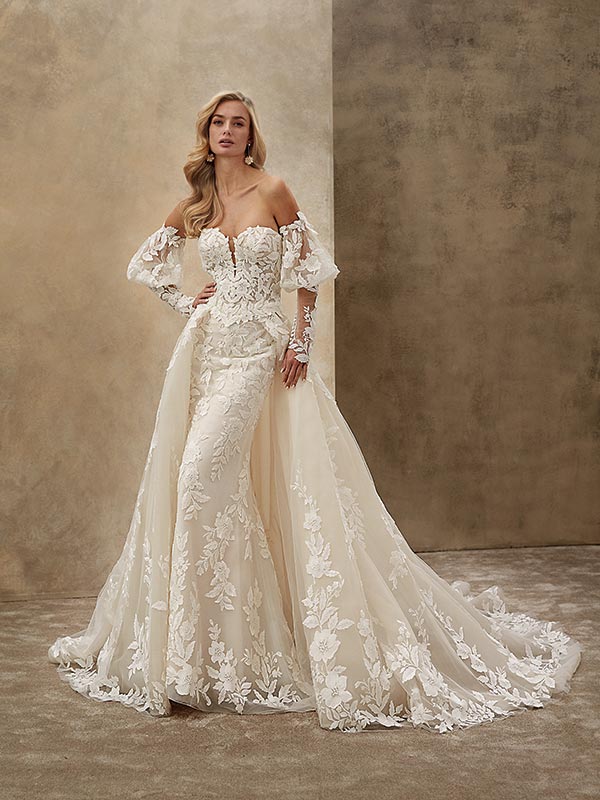 Junge Frau mit leichtem Lächeln trägt ein elegantes cremefarbenes Spitzenbrautkleid