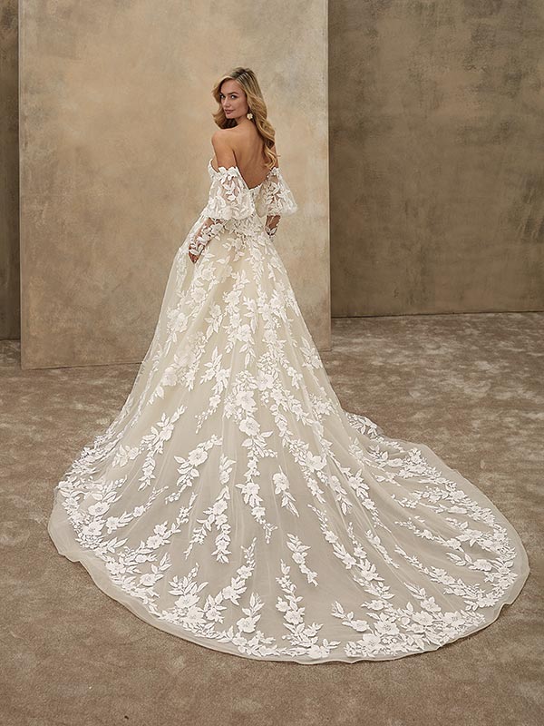 Eine blonde Frau mit freundlichem Gesichtsausdruck trägt ein cremefarbenes Spitzenkleid