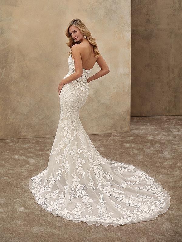 Eine blonde Frau lächelt leicht und trägt ein elegantes weißes Spitzenkleid mit Schleppe