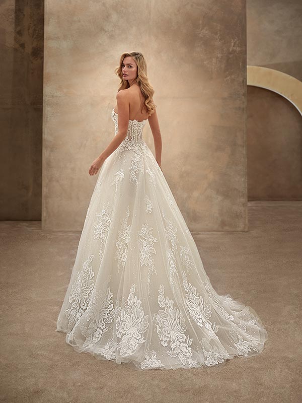 Junge Frau mit langen blonden Haaren trägt ein elegantes weißes Spitzenkleid und lächelt zurück