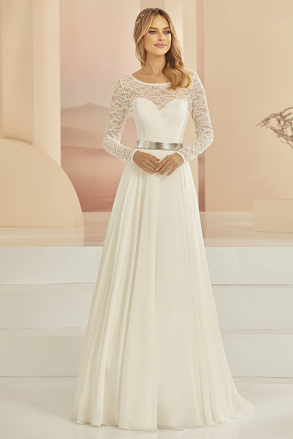 Junge Frau mit sanftem Lächeln trägt ein langes, cremeweißes Spitzenkleid