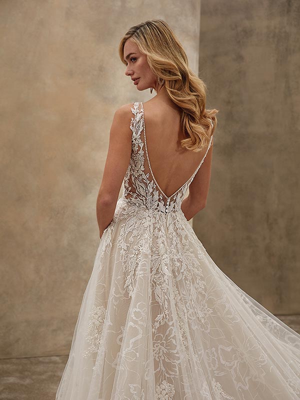 Eine blonde Frau mit sanftem Lächeln trägt ein weißes Spitzenkleid mit offenem Rücken