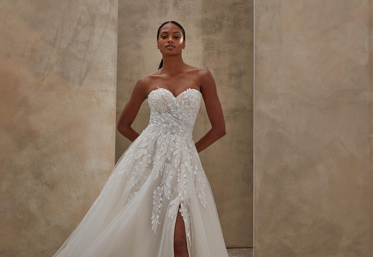 Eine junge Frau mit ernstem Blick trägt ein weißes Brautkleid mit Spitzenapplikationen