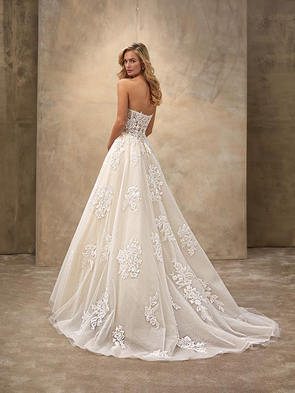 Blonde Frau im cremefarbenen Brautkleid mit Spitze lächelt über die Schulter