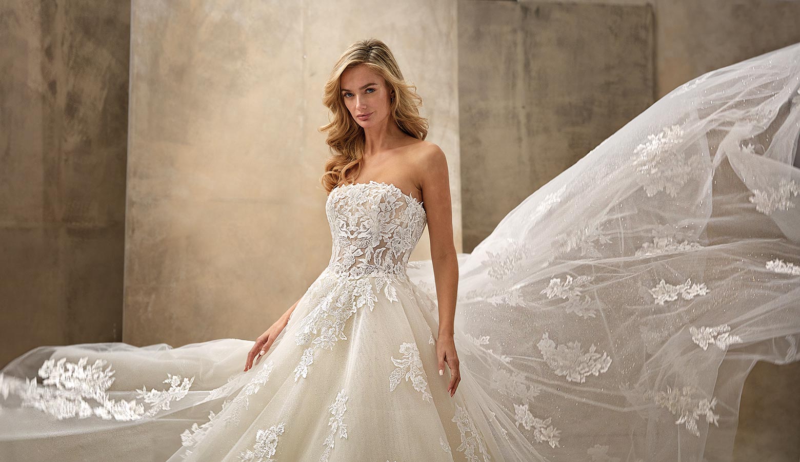 Eine blonde Frau mit ernstem Gesicht trägt ein elegantes cremefarbenes Brautkleid mit Spitzen und langem Schleier