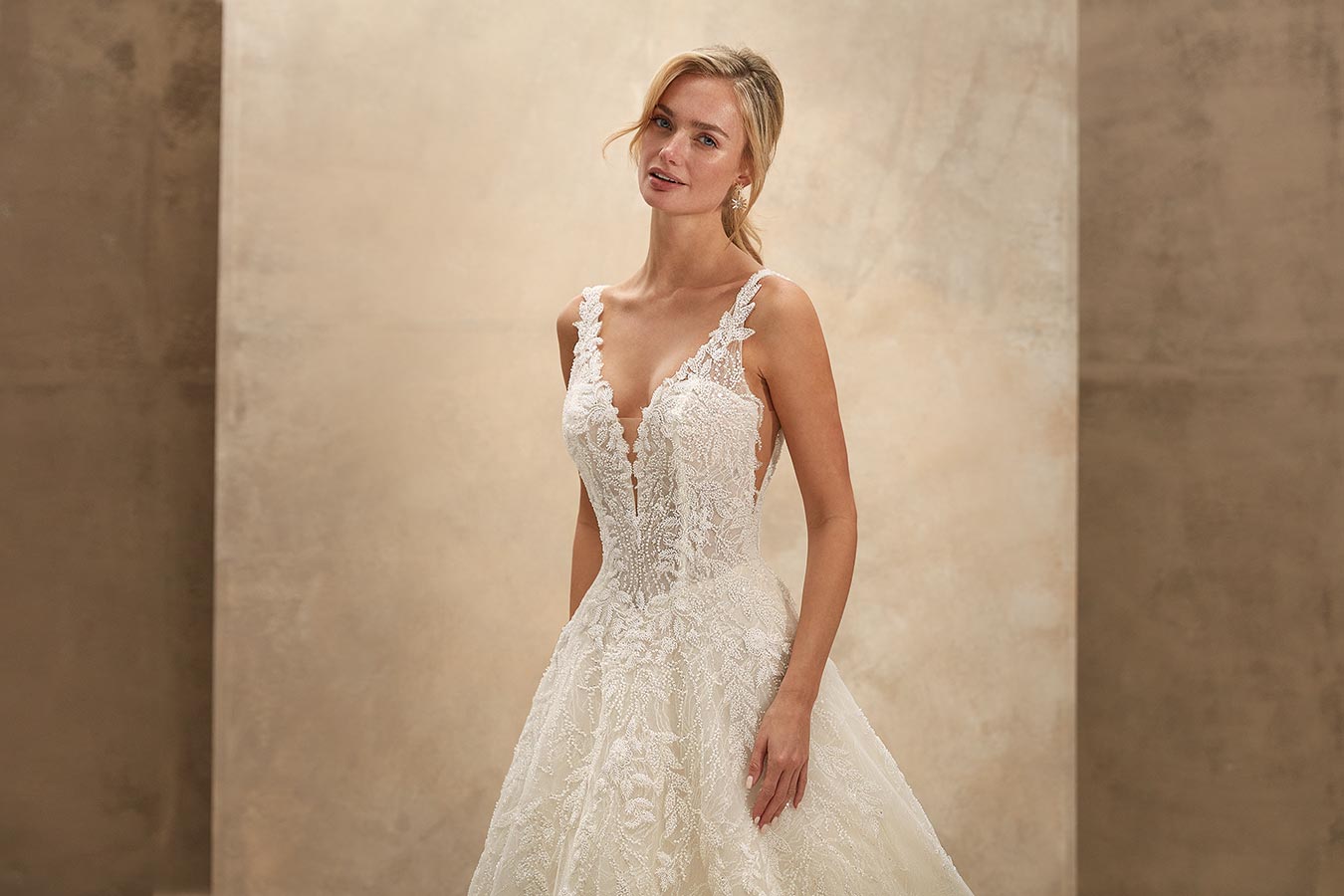 Blonde Frau lächelt leicht in einem eleganten cremefarbenen Spitzenbrautkleid