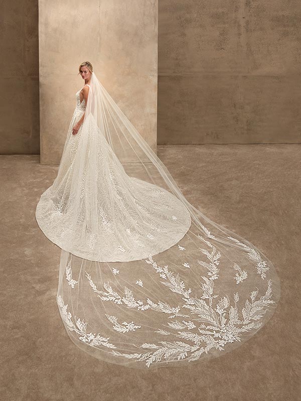 Eine Braut in cremefarbenem Kleid mit langem Schleier blickt elegant über die Schulter