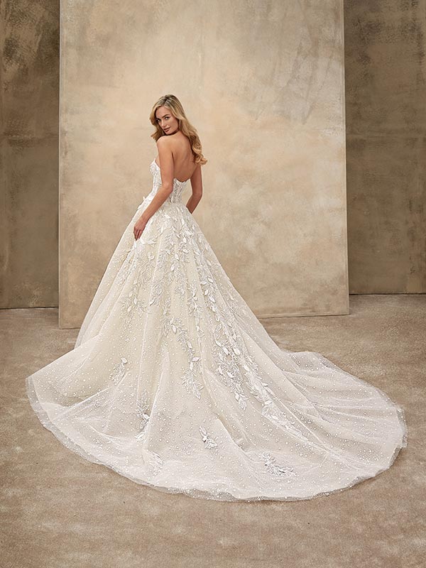 Eine blonde Frau lächelt dezent in weißem Glitzerkleid mit langer Schleppe