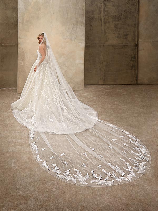 Eine lächelnde Braut im cremefarbenen Spitzenkleid mit langer transparenter Schleppe