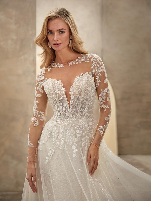 Eine blonde Frau lächelt zart in einem eleganten cremefarbenen Brautkleid mit Spitze