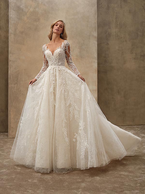 Blonde Frau mit sanftem Lächeln trägt ein weißes Spitzenbrautkleid mit langen Ärmeln