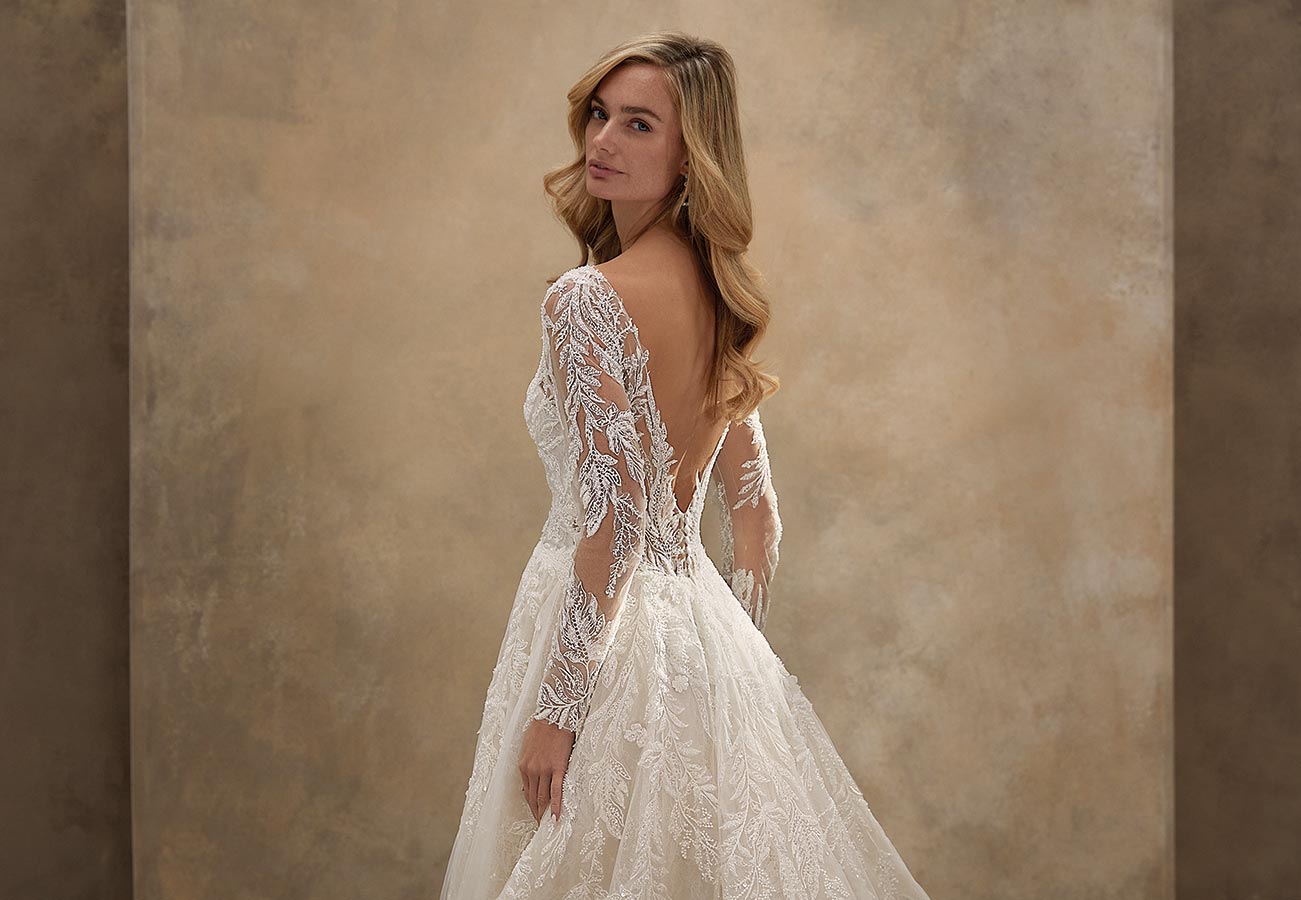 Eine blonde Frau mit sanftem Lächeln trägt ein elegantes weißes Spitzenkleid