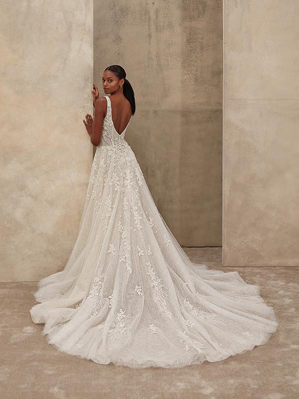 Eine elegante Frau mit ernstem Blick trägt ein weißes Spitzenkleid mit langer Schleppe