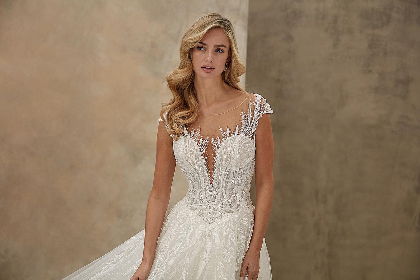 Eine blonde Frau in einem eleganten weißen Brautkleid mit feinen Spitzenmustern und sanftem Ausdruck