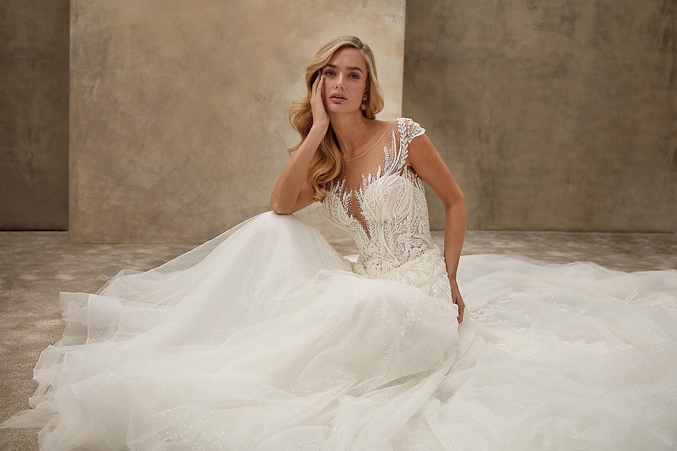 Eine blonde Frau sitzt nachdenklich in einem weißen, detailreichen Brautkleid