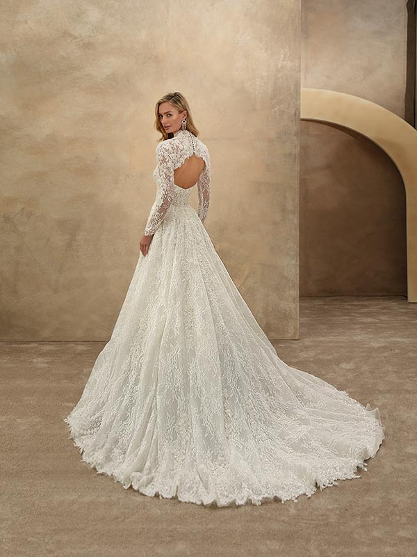 Eine blonde Frau im eleganten weißen Spitzenkleid mit offenem Rücken steht ruhig