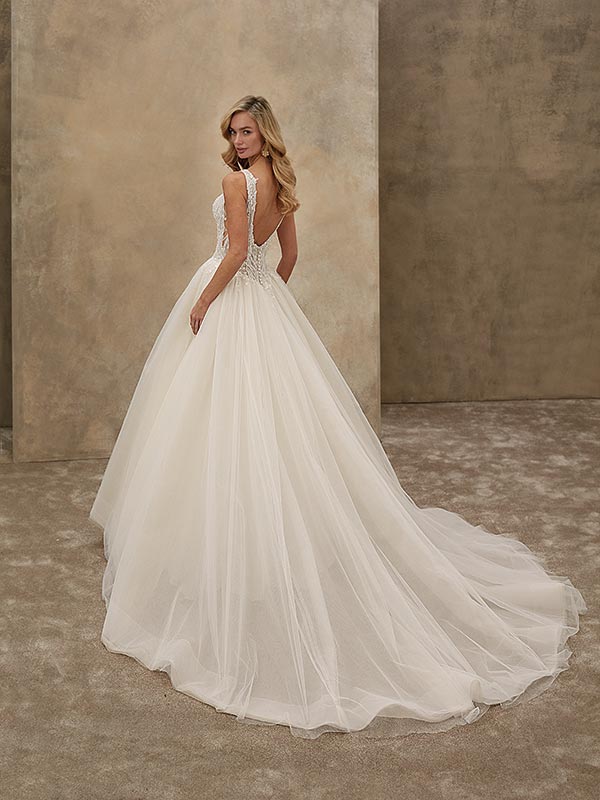 Eine blonde Frau im weißen Hochzeitskleid mit elegantem Rückenausschnitt lächelt leicht