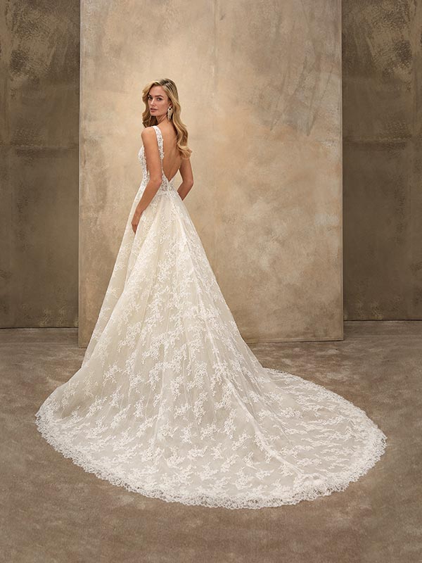 Eine blonde Frau lächelt leicht in einem cremeweißen Spitzen-Brautkleid mit Schleppe