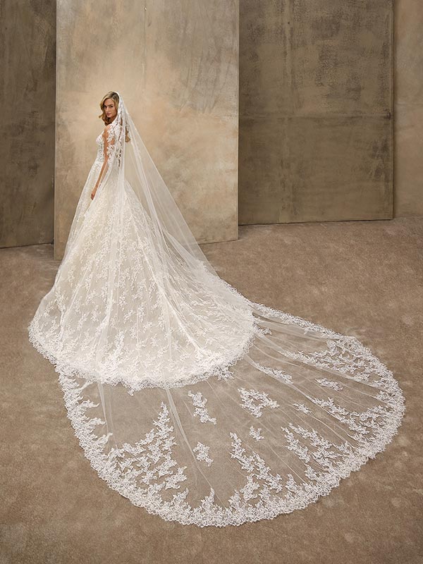 Eine Frau im eleganten weißen Brautkleid mit langem Schleier blickt ruhig zurück