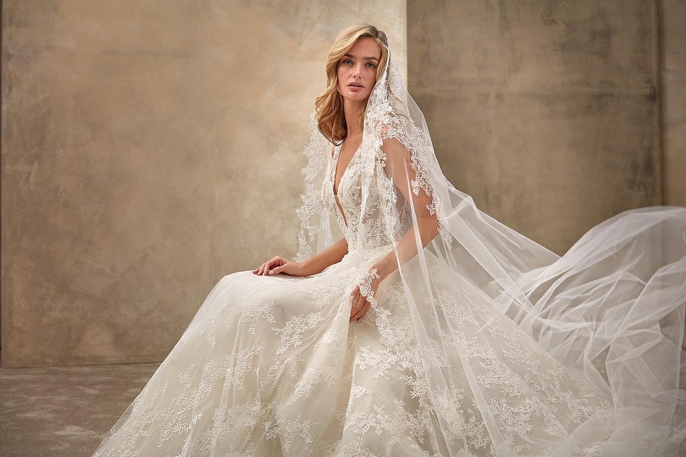 Eine blonde Frau mit sanftem Gesichtsausdruck trägt ein cremefarbenes Spitzenbrautkleid