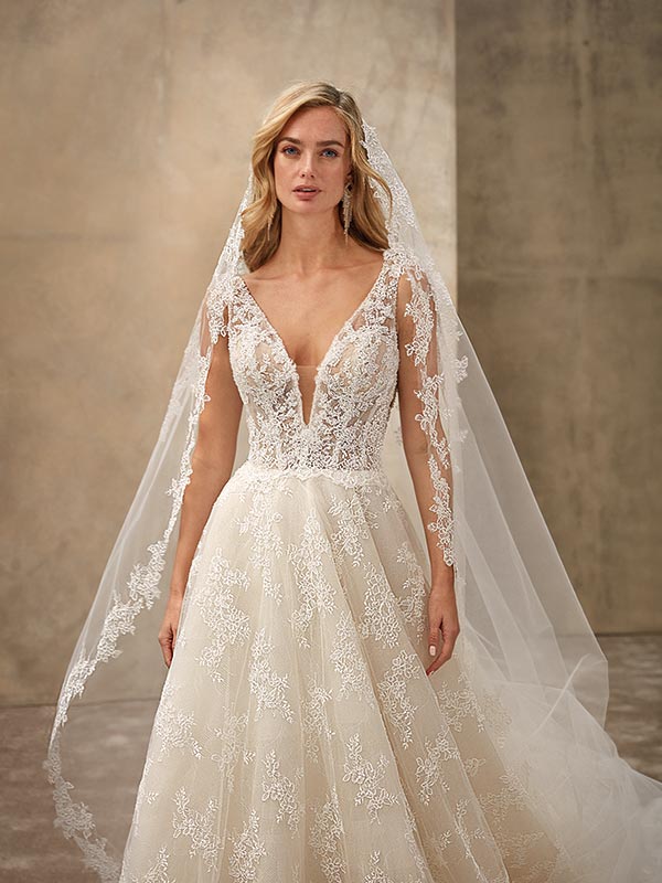 Eine blonde Frau mit ernstem Blick trägt ein elegantes weißes Brautkleid mit Spitze