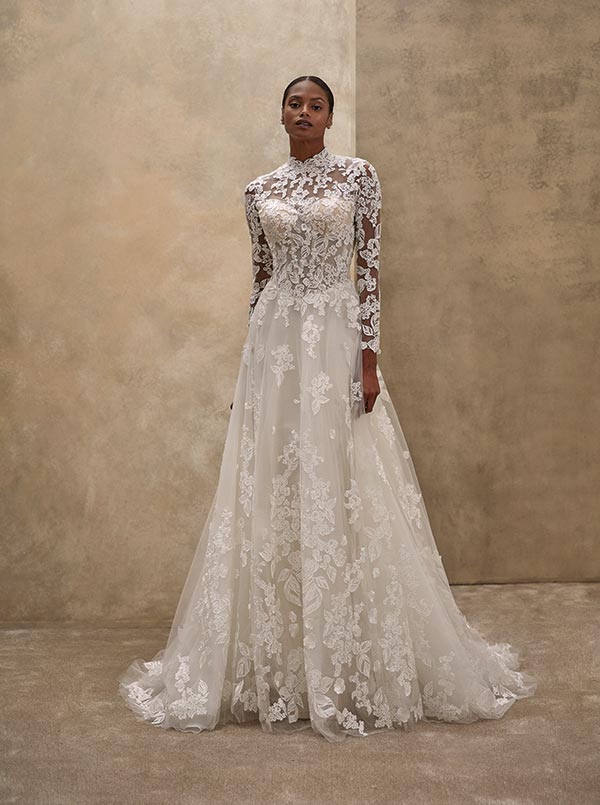 Eine elegante Frau im weißen Spitzenkleid steht ruhig vor beigem Hintergrund