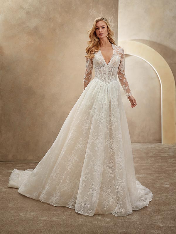 Eine Frau mit langen blonden Haaren trägt ein elegantes Spitzenbrautkleid in Weiß