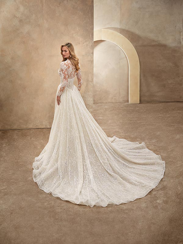 Eine Frau mit langen blonden Haaren trägt ein elfenbeinfarbenes Spitzenkleid und blickt elegant über die Schulter