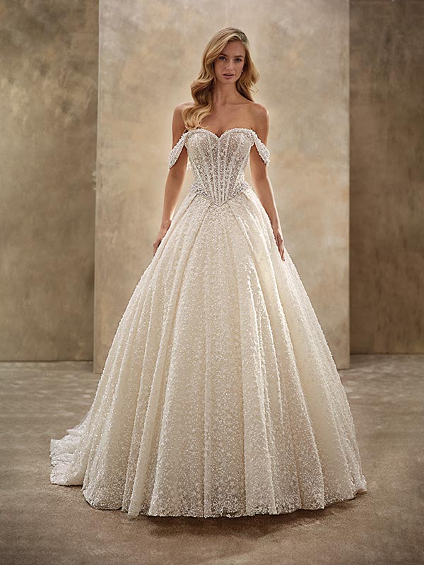 Eine blonde Frau mit sanftem Lächeln trägt ein cremefarbenes funkelndes Brautkleid