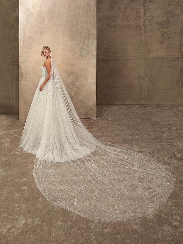 Eine blonde Frau im weißen Brautkleid mit langem Schleier blickt ernst zurück