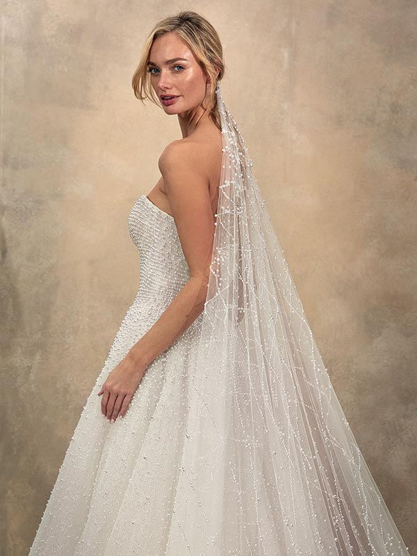 Eine blonde Frau im eleganten weißen Brautkleid mit Perlendetails lächelt sanft