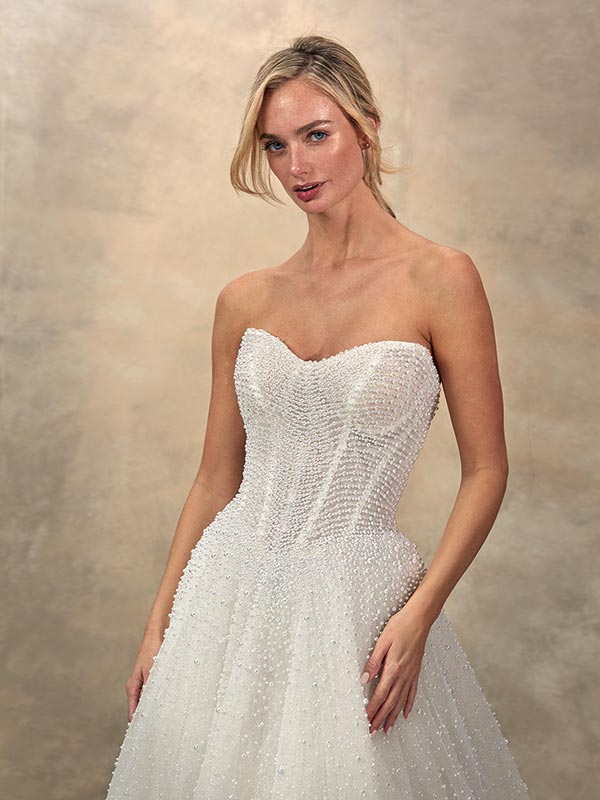 Eine blonde Frau mit zartem Lächeln trägt ein glitzerndes weißes Brautkleid