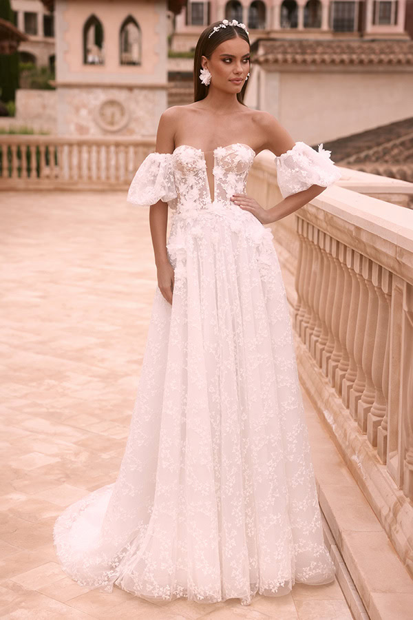 Eine lächelnde Frau im eleganten weißen Brautkleid mit floraler Spitze und Puffärmeln