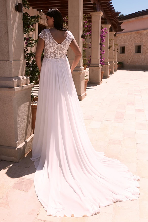 Eine Frau im weißen Brautkleid mit Spitze am Rücken steht elegant im Sonnenschein