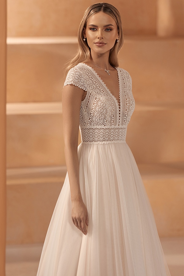 Eine junge Frau mit sanftem Lächeln in cremefarbenem Brautkleid mit Spitzenoberteil