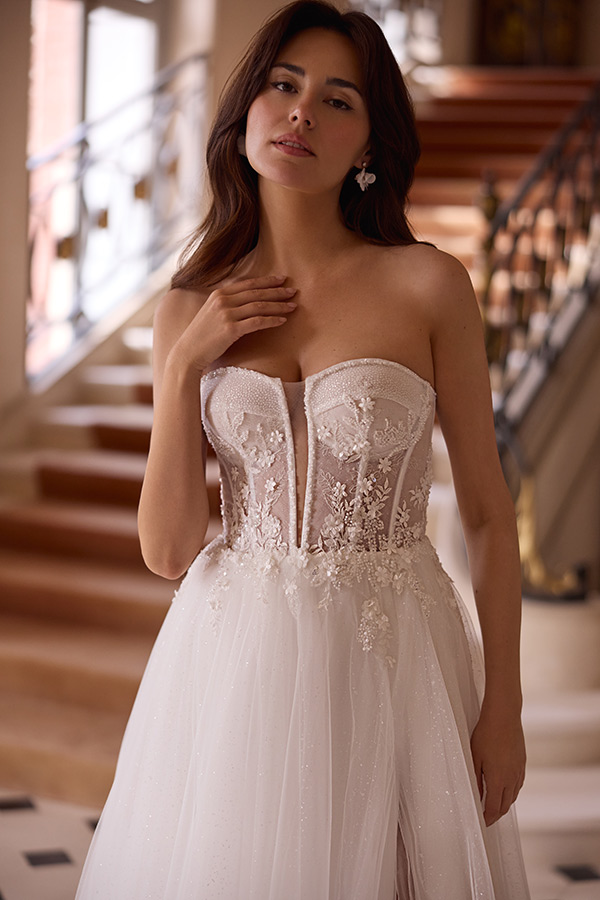 Junge Frau mit langen braunen Haaren trägt ein elegantes weißes Brautkleid und wirkt verträumt