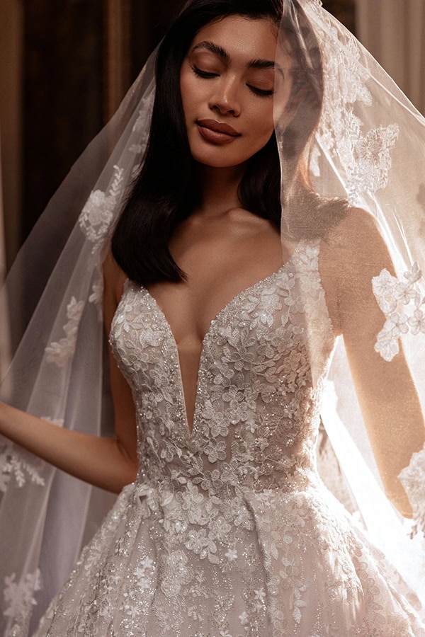 Eine Frau mit dunklem Haar lächelt sanft in einem eleganten, weißen Brautkleid